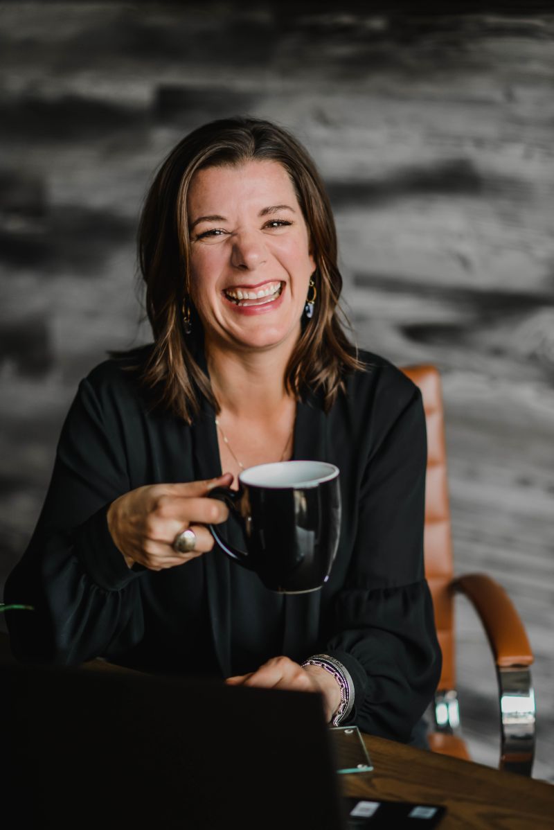 Andrea Binoniemi smiling and holding a coffee mug at a table.